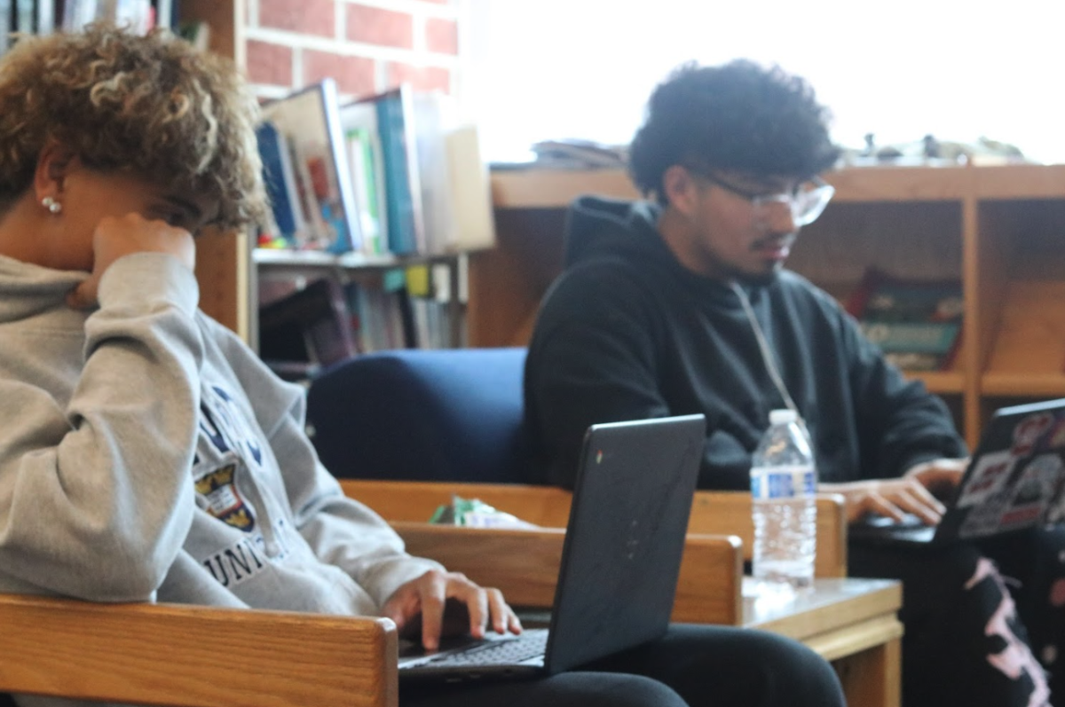 Two students work on assignments while sharing food while in the back of the library.